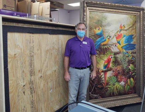 Oversized framed painting of tropical birds beside custom-built wood crate — expert art packing and shipping services in New Orleans