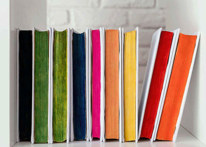 A line of colorful books binded by gentilly mail and copy center lying on a shelf.